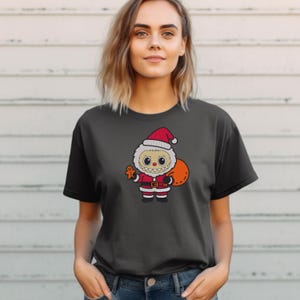 Woman wearing a black t-shirt with a Santa monster embroidery design, holding a gift bag and gingerbread cookie – Christmas-themed digital embroidery mockup