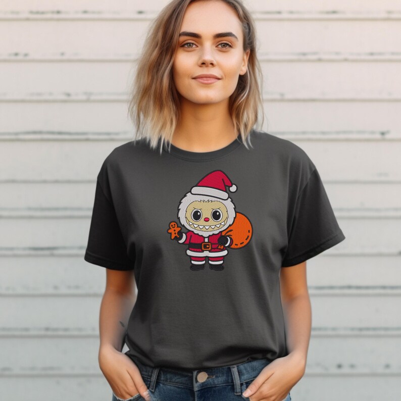 Woman wearing a black t-shirt with a Santa monster embroidery design, holding a gift bag and gingerbread cookie – Christmas-themed digital embroidery mockup