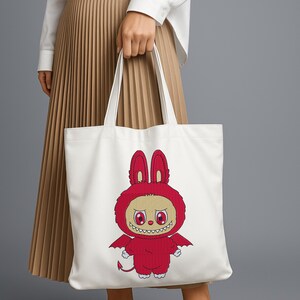 White tote bag with a red devil bunny monster embroidery design, held by a woman wearing a pleated skirt – shown as a mockup for a digital embroidery file download