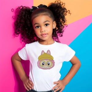 Little girl in white t-shirt featuring pink kawaii monster bunny embroidery with yellow hat – cute kids digital embroidery mockup