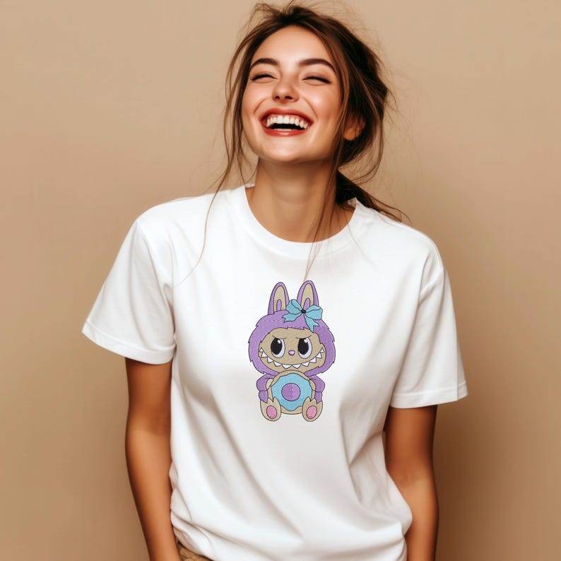 Woman wearing a white t-shirt with a purple kawaii monster embroidery design holding a blue egg, styled as a mockup for digital machine embroidery download