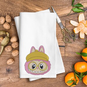 White tea towel with pink kawaii monster bunny embroidery wearing yellow hat and glasses – cute home decor embroidery mockup