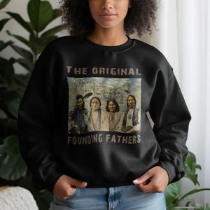 Peut inclure: Sweat-shirt noir avec l'inscription "THE ORIGINAL FOUNDING FATHERS" au-dessus d'une image de figures amérindiennes et du Mont Rushmore. Le sweat-shirt est de style col rond.