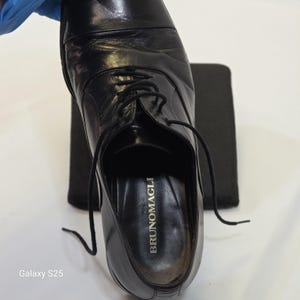 Puede incluir: Un zapato oxford de cuero negro con dise&ntilde;o de puntera y cordones negros finos. La plantilla interior presenta el nombre de la marca BRUNOMAGLI impreso en letras doradas. El zapato tiene un acabado liso y pulido con una forma de puntera redondeada.