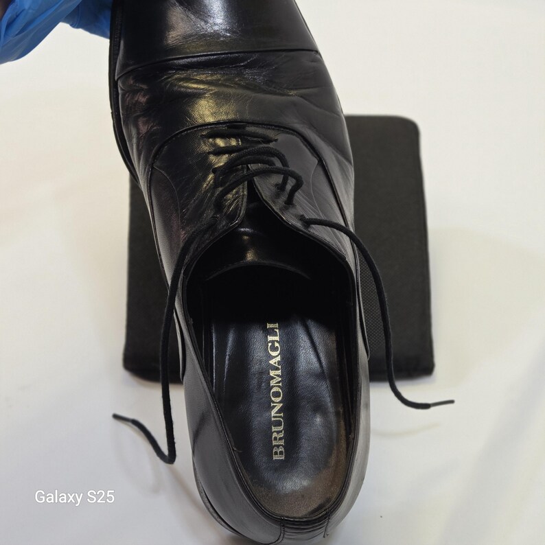 Puede incluir: Un zapato oxford de cuero negro con dise&ntilde;o de puntera y cordones negros finos. La plantilla interior presenta el nombre de la marca BRUNOMAGLI impreso en letras doradas. El zapato tiene un acabado liso y pulido con una forma de puntera redondeada.
