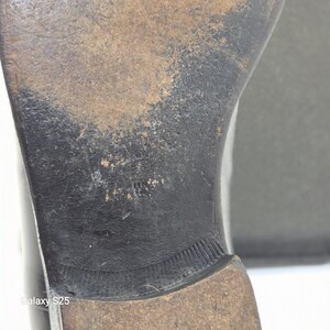 Puede incluir: La suela de cuero negro de un zapato que muestra signos de desgaste, con un tac&oacute;n marr&oacute;n oscuro y una superficie texturizada. La suela presenta un acabado desgastado con rasgu&ntilde;os y ara&ntilde;azos visibles en el centro y el tac&oacute;n.