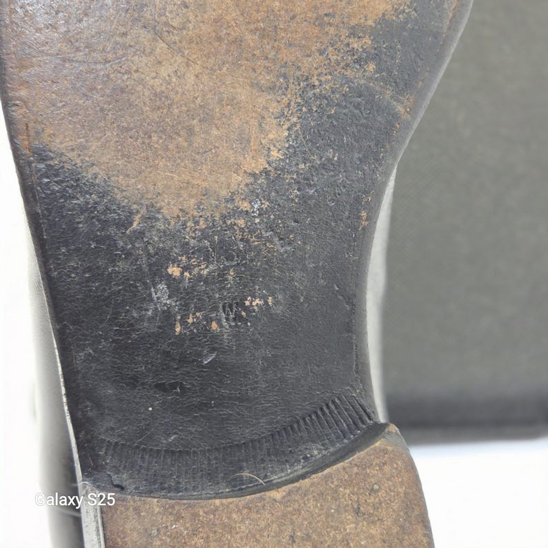 Puede incluir: La suela de cuero negro de un zapato que muestra signos de desgaste, con un tac&oacute;n marr&oacute;n oscuro y una superficie texturizada. La suela presenta un acabado desgastado con rasgu&ntilde;os y ara&ntilde;azos visibles en el centro y el tac&oacute;n.