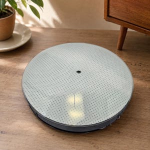 May include: A circular, low-profile ceiling light fixture featuring a white, semi-translucent cover with a dense pattern of small, dark dots. The fixture has a smooth, flat surface with a single, small, dark circular opening centered at the top.