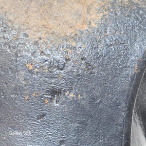 Puede incluir: Una suela de zapato negra y texturizada con desgaste y suciedad visibles. La suela presenta un sello en relieve con el texto '10' sobre la letra 'W'. La superficie es irregular, mostrando signos de uso con rozaduras y material desgastado.