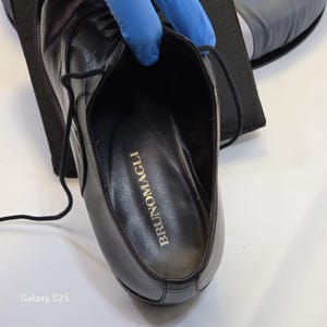 Puede incluir: Un zapato de cordones de cuero negro con acabado liso y cordones negros finos. La plantilla interior es negra y presenta el nombre de la marca BRUNOMAGLI impreso en letras doradas. El zapato tiene un tal&oacute;n estructurado y una puntera redondeada.