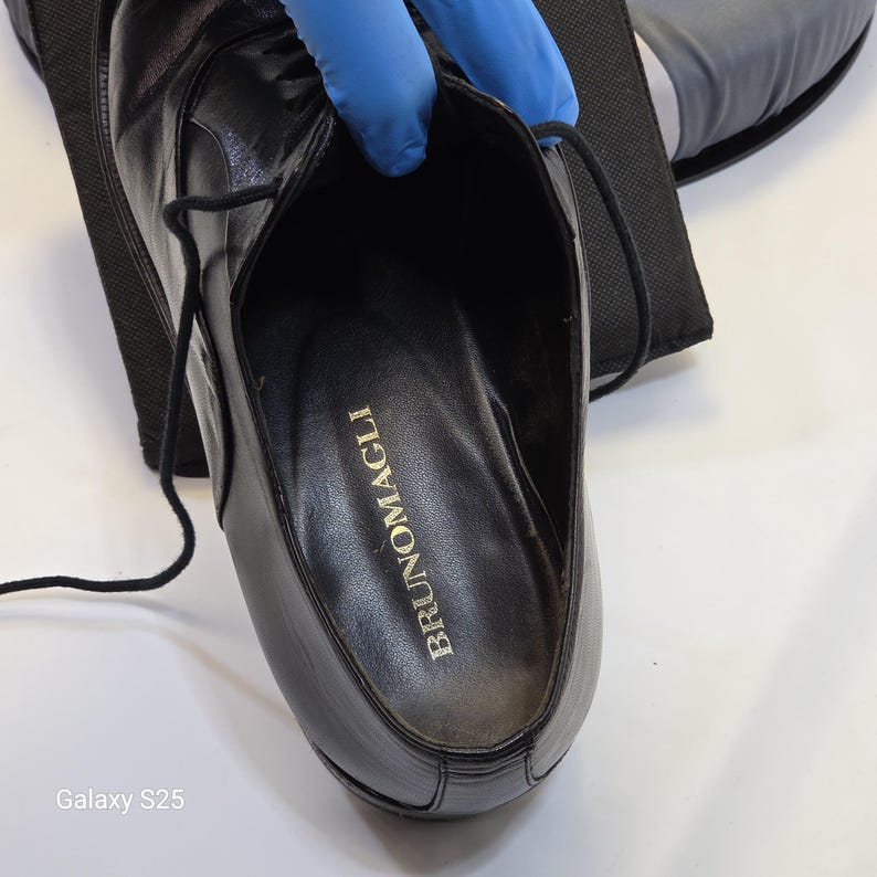 Puede incluir: Un zapato de cordones de cuero negro con acabado liso y cordones negros finos. La plantilla interior es negra y presenta el nombre de la marca BRUNOMAGLI impreso en letras doradas. El zapato tiene un tal&oacute;n estructurado y una puntera redondeada.
