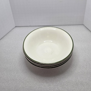 May include: A stack of four white ceramic bowls with a dark green trim around the rim. The bowls are stacked on top of each other, with the top bowl facing up. The bowls are on a light gray surface.