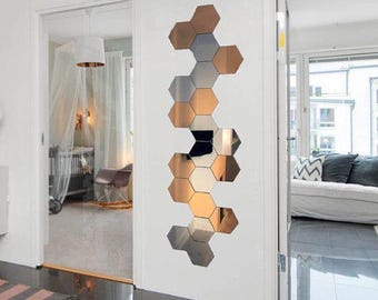 May include: A decorative wall mirror composed of hexagonal tiles in shades of copper, silver, and black. The geometric design is mounted vertically on a white wall, reflecting the room's interior.