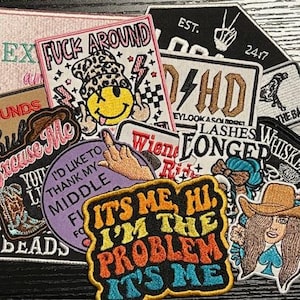 May include: A collection of embroidered patches with various designs and text. The patches feature phrases like "Fuck Around," "It's Me, Hi, I'm the Problem, It's Me," and images of a cowboy hat, a middle finger, and a smiley face.