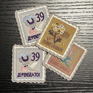May include: Four embroidered patches in the shape of postage stamps. Two stamps feature a floral design with the text "BONNE COURAGE" and "BONNE CHANCE". The other two stamps have a floral design with the text "JE PENSE A TOI" and the number "39".