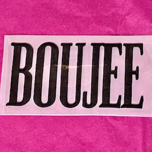 May include: A white rectangular sticker with the word "BOUJEE" in bold, black capital letters. The sticker is set against a vibrant pink background.