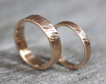 May include: Two rose gold wedding bands with a textured finish. The bands are stacked on top of each other.