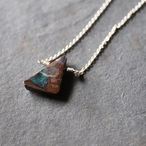 Pode incluir: Um colar de corrente de prata com um pingente de opala triangular. A opala &eacute; de cor marrom escura com flashes iridescentes verdes e azuis.
