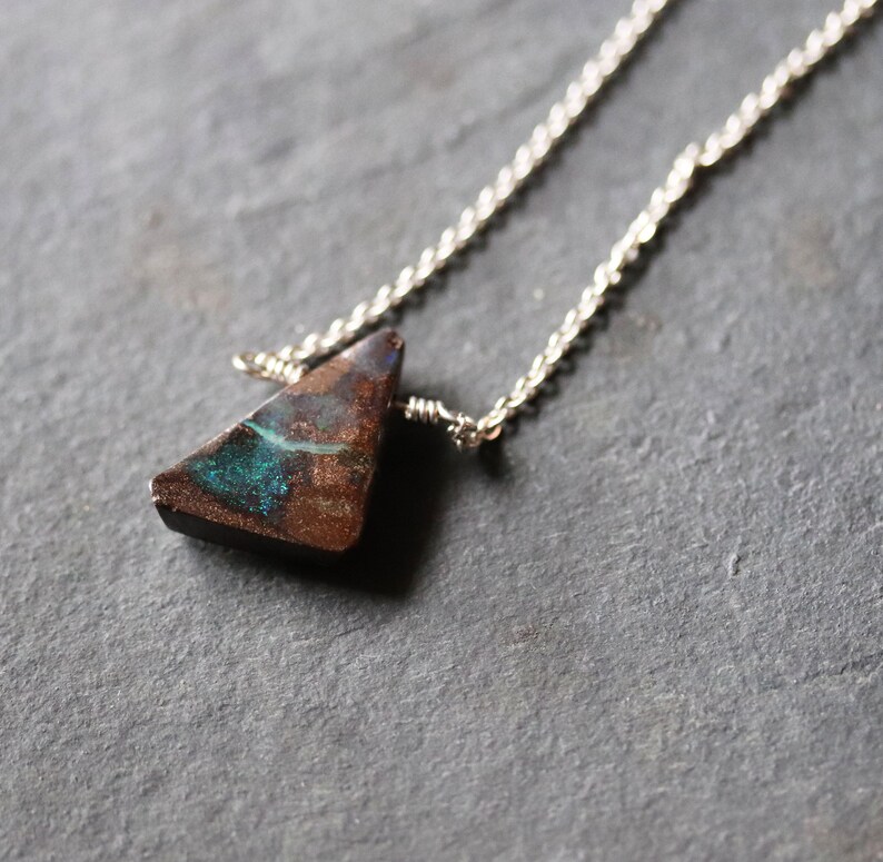 Pode incluir: Um colar de corrente de prata com um pingente de opala triangular. A opala &eacute; de cor marrom escura com flashes iridescentes verdes e azuis.