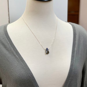 Pode incluir: Um colar de corrente de prata com um pingente em forma de l&aacute;grima azul escuro.
