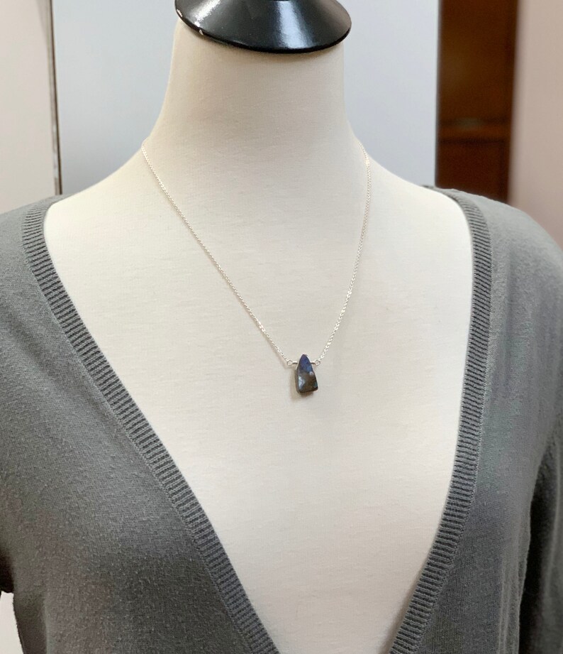 Pode incluir: Um colar de corrente de prata com um pingente em forma de l&aacute;grima azul escuro.