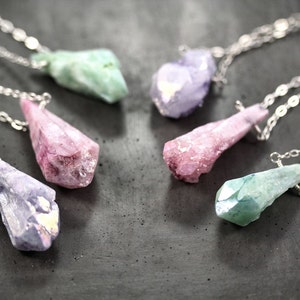 Puede incluir: Cinco collares de cristal con cadenas plateadas. Los cristales son de varias formas y colores, incluyendo verde, morado y rosa.