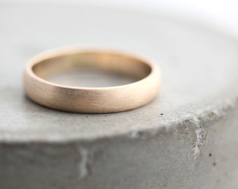 May include: A simple, brushed gold wedding band. The band is smooth and has a matte finish.