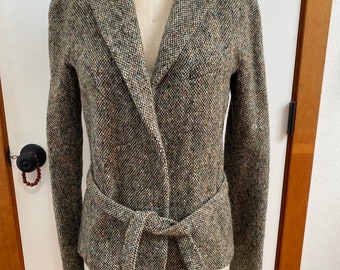 May include: A tweed jacket with a wrap-style front and a matching belt tied at the waist. The jacket is displayed on a mannequin and features a mix of brown, beige, and blue threads. The mannequin has the text "ROYAL FORM" on the top.