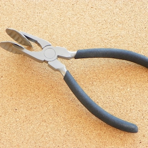 May include: Silver pliers with black rubber handles. The pliers have a unique design with a curved jaw.