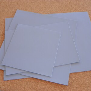 May include: Four sheets of light blue thermal pad material stacked on top of each other.