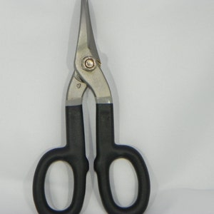 May include: A pair of black handled metal shears with a silver finish. The shears have a small triangle symbol on the top of the blade.