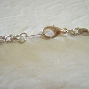 May include: Close-up of a gold-colored lobster clasp and a silver-colored chain necklace. The chain links are oval-shaped. The clasp is attached to a small ring connected to the chain.