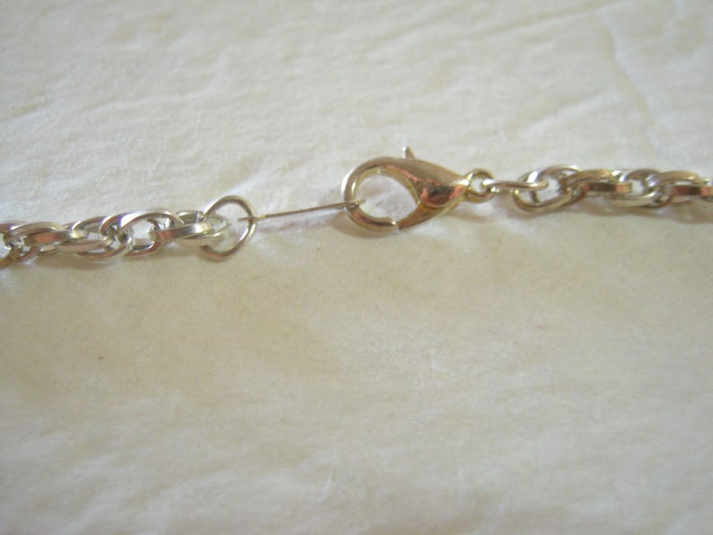May include: Close-up of a gold-colored lobster clasp and a silver-colored chain necklace. The chain links are oval-shaped. The clasp is attached to a small ring connected to the chain.