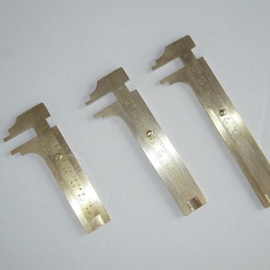 May include: Three silver-colored metal calipers with different sizes. The calipers have a measurement scale in inches.