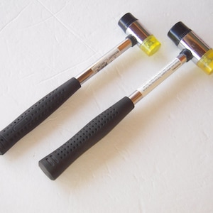 May include: Two rubber mallets with black rubber handles and yellow rubber heads. The mallets are made of metal and have a silver finish.