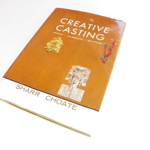 May include: A brown book titled "Creative Casting: Jewelry, Silverware, Sculpture" by Sharr Choate. The book cover features three small sculptures.