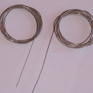 May include: Two spools of silver wire, one is coiled and the other is straight.