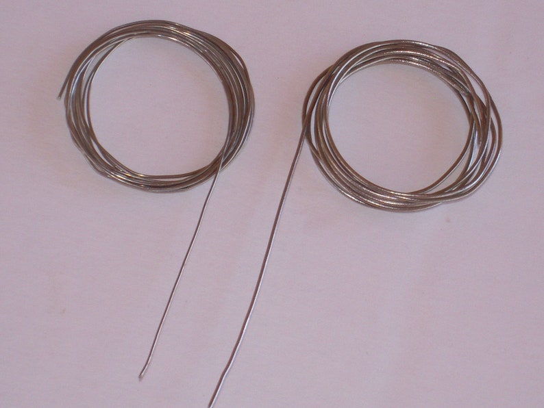 May include: Two spools of silver wire, one is coiled and the other is straight.
