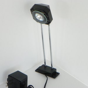 May include: A black and silver adjustable desk lamp with a clear glass shade. The lamp is plugged into a black power adapter.