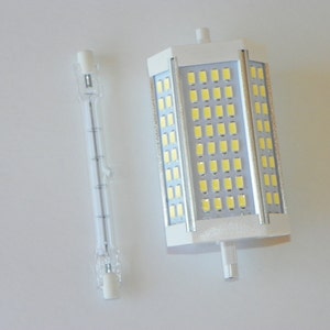 May include: A comparison of two light bulbs. A standard incandescent light bulb and a larger LED light bulb with a white plastic housing and a grid of small white LED lights.