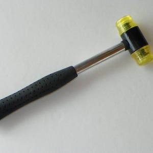 May include: A yellow rubber mallet with a black handle and a textured grip. The mallet is made of durable plastic and is ideal for a variety of tasks.