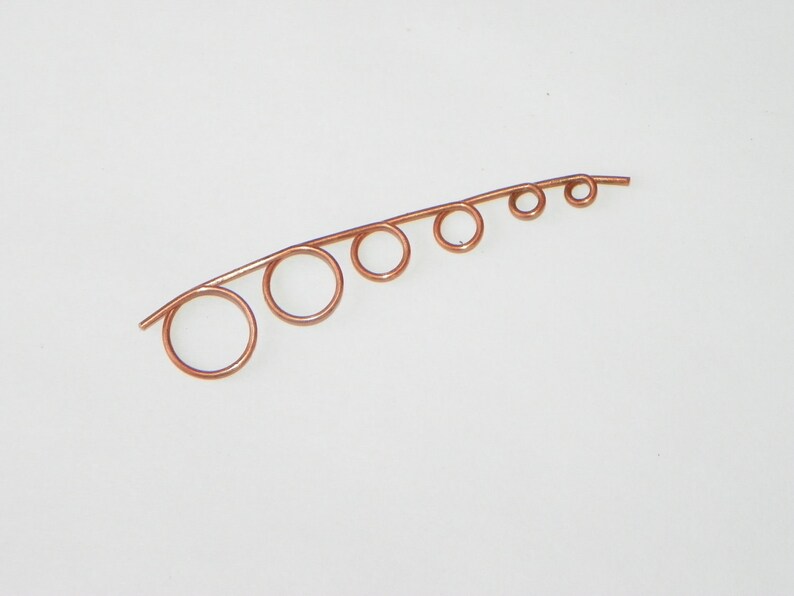 May include: A copper wire with five loops of varying sizes, creating a graduated effect. The wire is bent into a curved shape.