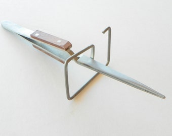 May include: A silver metal tweezers with a brown wooden handle is resting on a silver metal stand. The tweezers are pointed and have a long, thin blade.