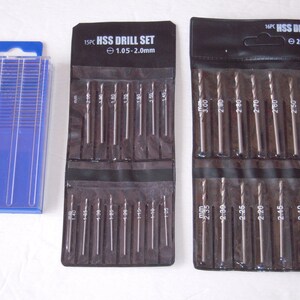 May include: Two sets of drill bits in black plastic packaging. The set on the left contains 15 drill bits ranging in size from 1.05 to 2.0 mm. The set on the right contains 16 drill bits ranging in size from 2.0 to 3.0 mm.