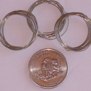 May include: Three spools of silver wire, each wound into a circle, next to a US quarter coin with the Kansas state quarter design featuring a buffalo and the text "Kansas 1861 2005 E Pluribus Unum".