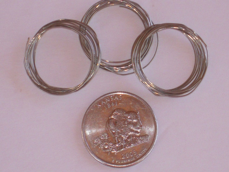May include: Three spools of silver wire, each wound into a circle, next to a US quarter coin with the Kansas state quarter design featuring a buffalo and the text "Kansas 1861 2005 E Pluribus Unum".