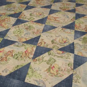 May include: A patchwork quilt featuring a repeating pattern of diamond-shaped fabric pieces. The fabric displays illustrations of Winnie the Pooh characters in a forest setting, alternating with solid dark blue textured fabric segments.