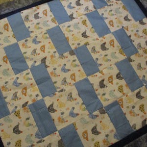 May include: A patchwork quilt with a repeating pattern of whimsical animal figures in various colors on a cream background. The quilt features blue rectangular blocks and a dark blue border.