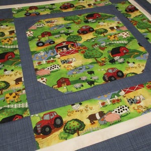 May include: A patchwork quilt featuring a central panel and border strips with a farm-themed print on a green background, depicting red barns, tractors, cows, pigs, sheep, and chickens. The fabric pieces are separated by solid blue and white borders.
