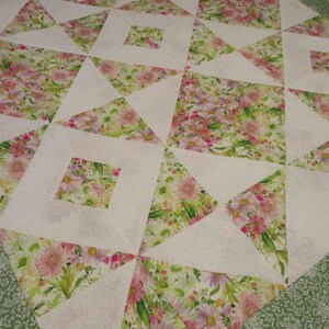 May include: A handmade quilt with a floral pattern. The quilt features white squares and triangles, with floral print squares in pink, green, and yellow. The border is a green floral print.
